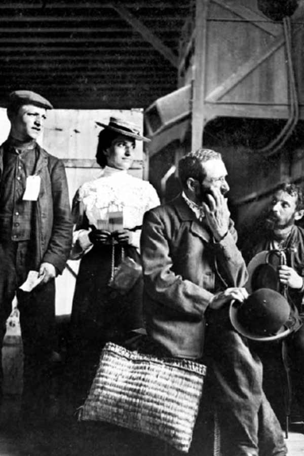 Black and white photo of a group of five immigrants sitting on a dock